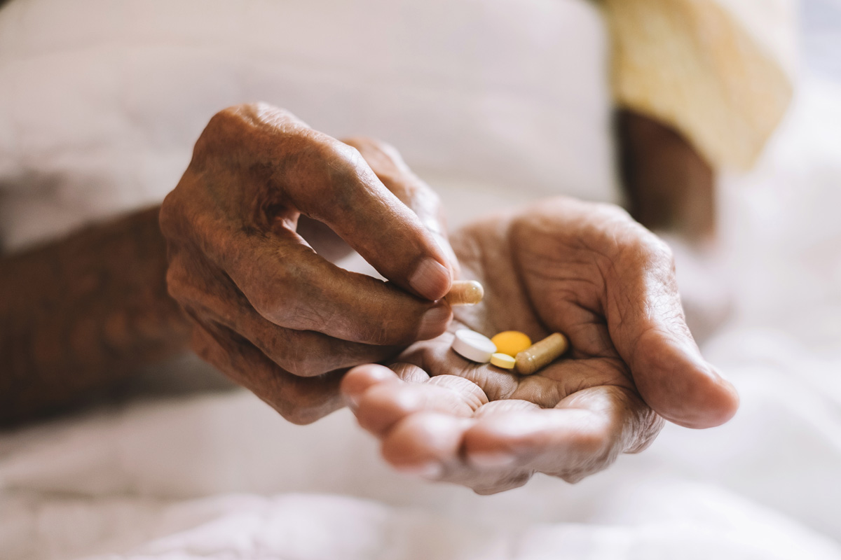 A close-up of an elderly person’s hands holding various pills.